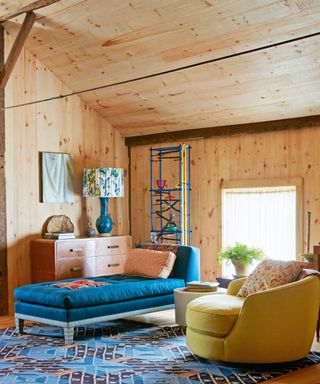 seating area with pine cladding blue daybed, yellow curved armchair and blue patterned rug