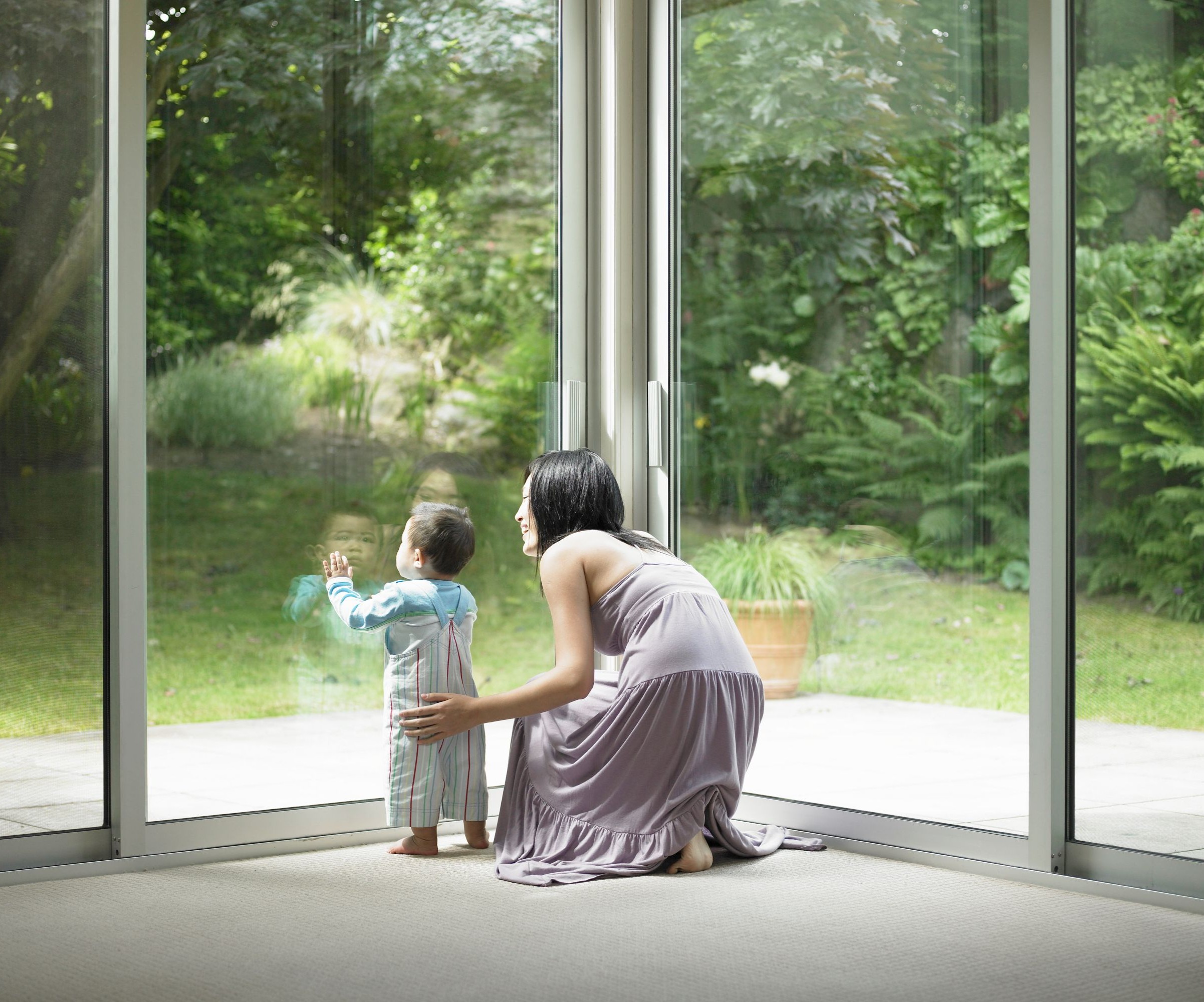 A mother and toddler son looking out at a garden through a large window
