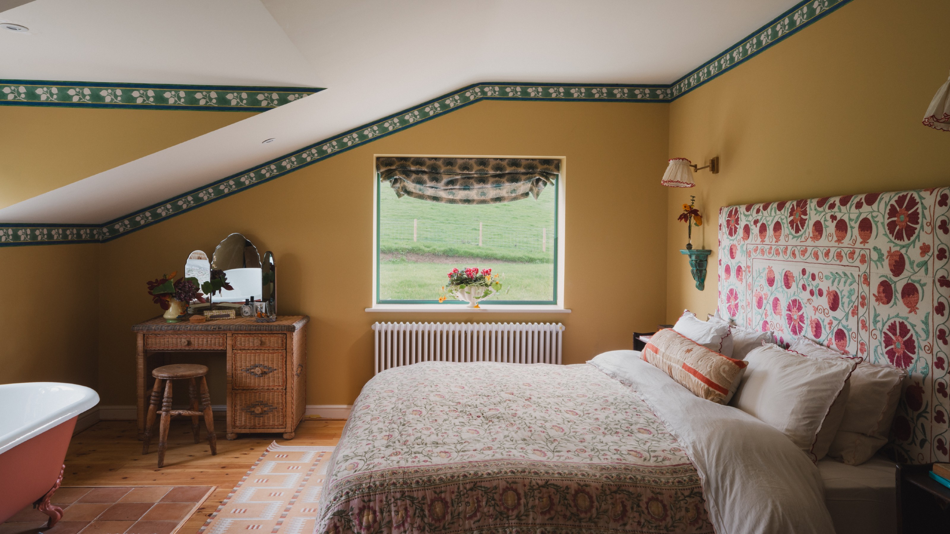 A mustard yellow-painted bedroom with a white slanted ceiling and a green floral trim by the ceiling