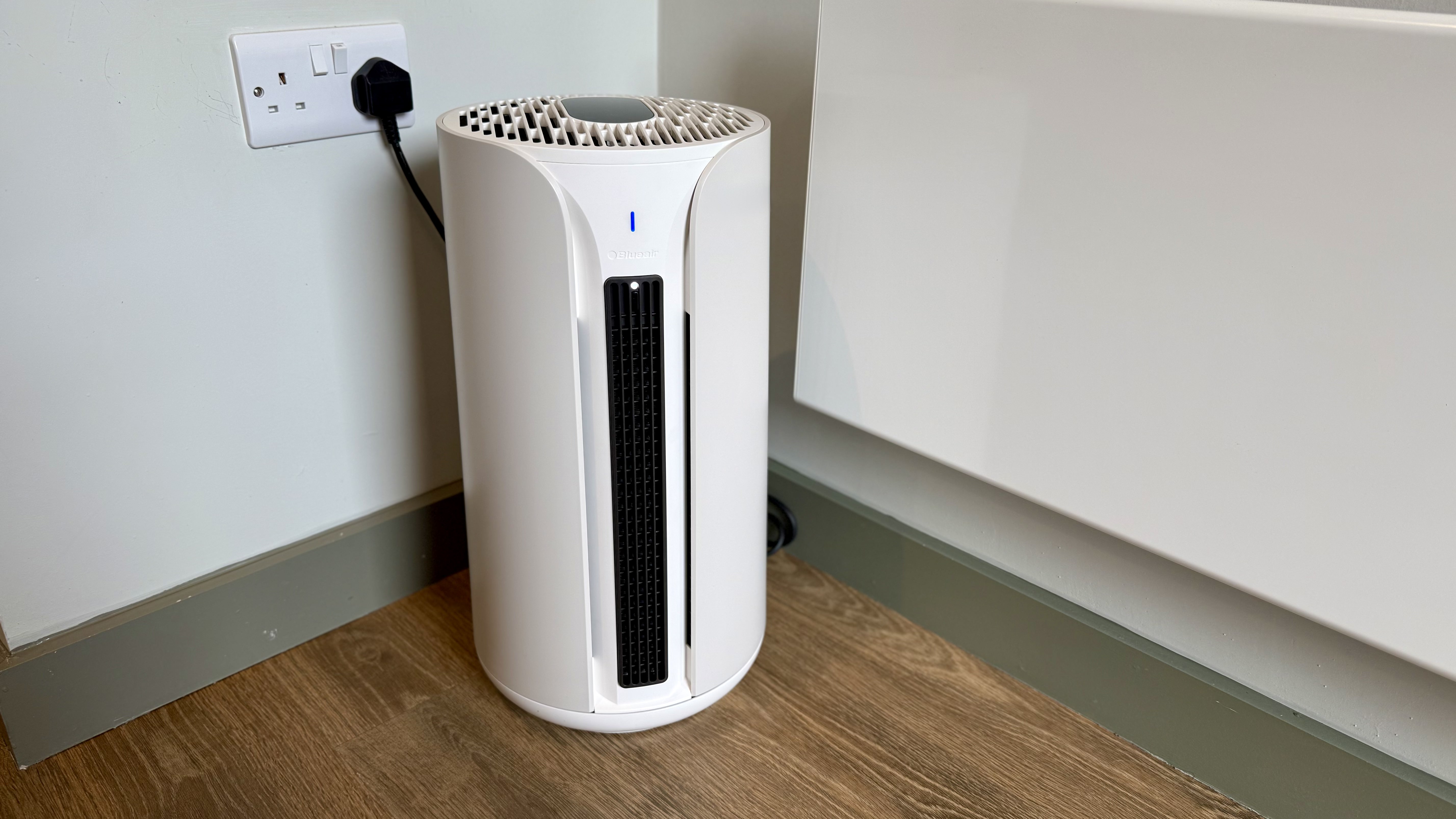 A photo of the Blueair T20i Air Purifier with its remote in a room with white walls and laminated wooden floors