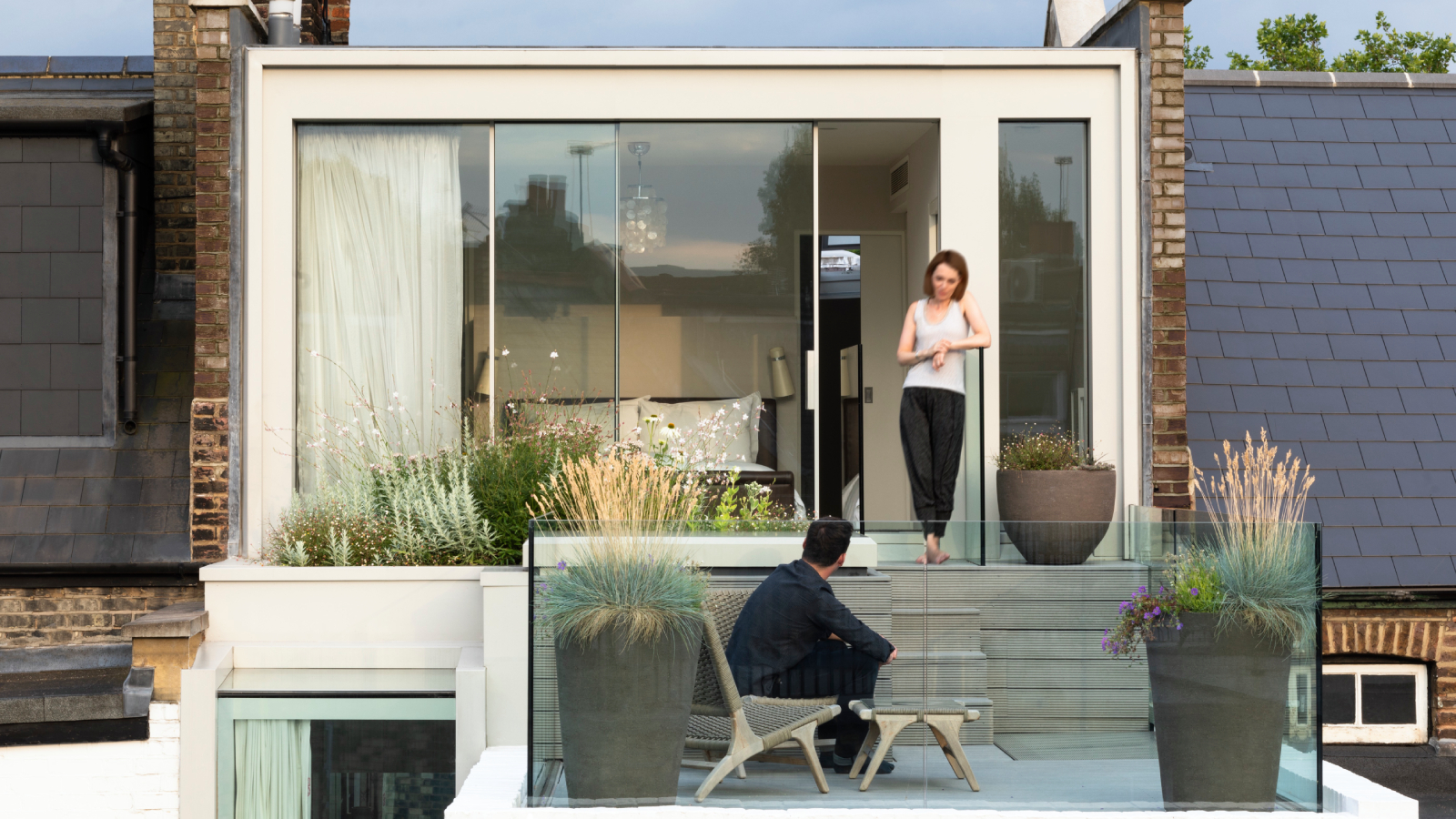 cream coloured loft conversion with sliding patio doors leading to roof terrace with planted areas and glass balustrade