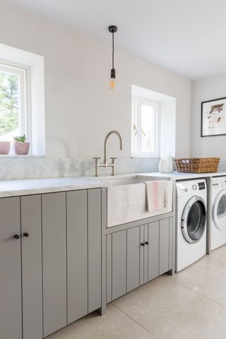 A utility room with grey panelled cabinets and white marble worktops.