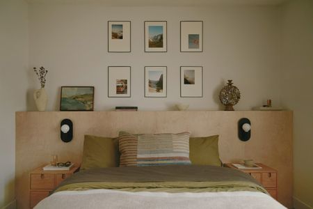 a bedroom with a plywood headboard and family photos on the wall behind, with green bedding on the bed