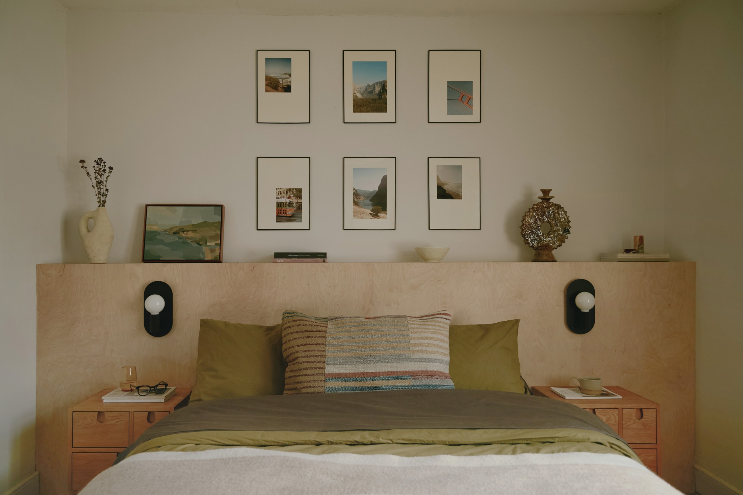 a bedroom with a plywood headboard and family photos on the wall behind, with green bedding on the bed
