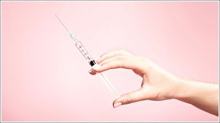 Hand holding syringe in plain pink background