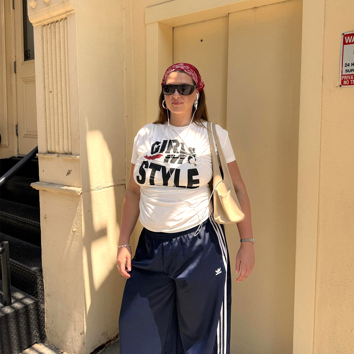 Influencer Raeann Langas wears Adidas track pants with a graphic tie and black sunglasses. 