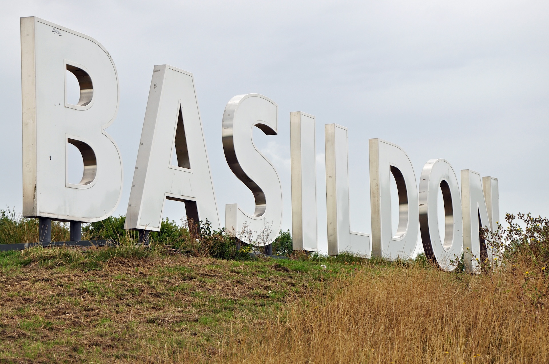 Large iconic road or town sign on small grassy hill outside new town. Near A127 trunk road. Capital letters. Outdoors on overcast autumn day