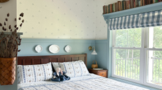 a bedroom with blue bedding, blue painted walls, stamped wall design, gingham blinds, and a bookshelf over the window