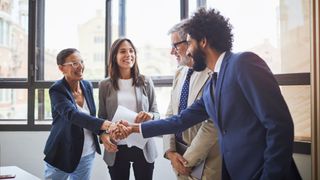 A diverse group of businesspeople shake hands in a boardroom