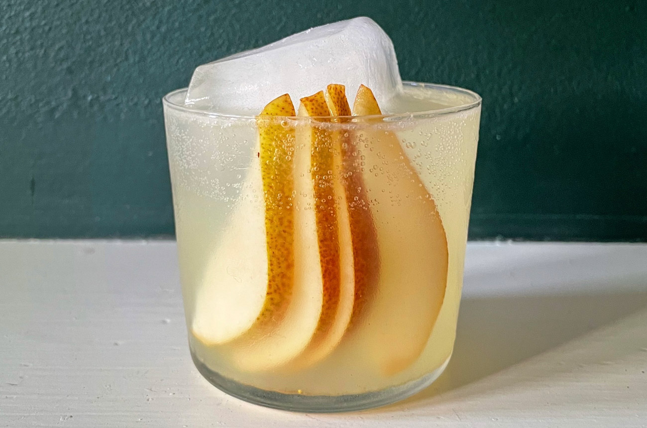 A cocktail in a short tumbler with a pear garnish