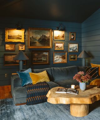 cozy snug room with dark teal walls, velvet sofa, wooden sculptural coffee table, gallery wall with vintage-style artwork