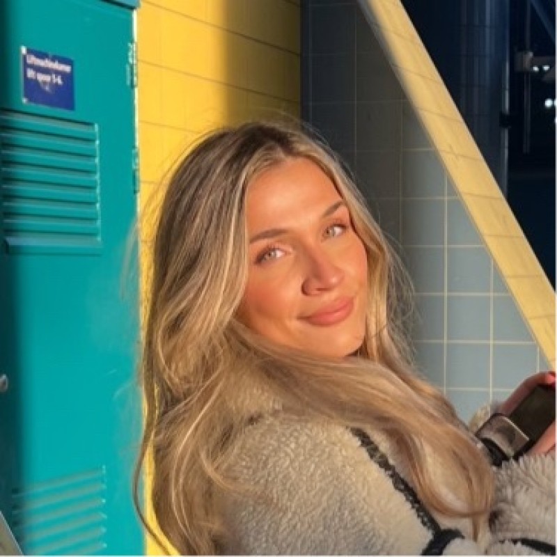 A young blonde woman smiling at the camera holding a DSLR in her hands