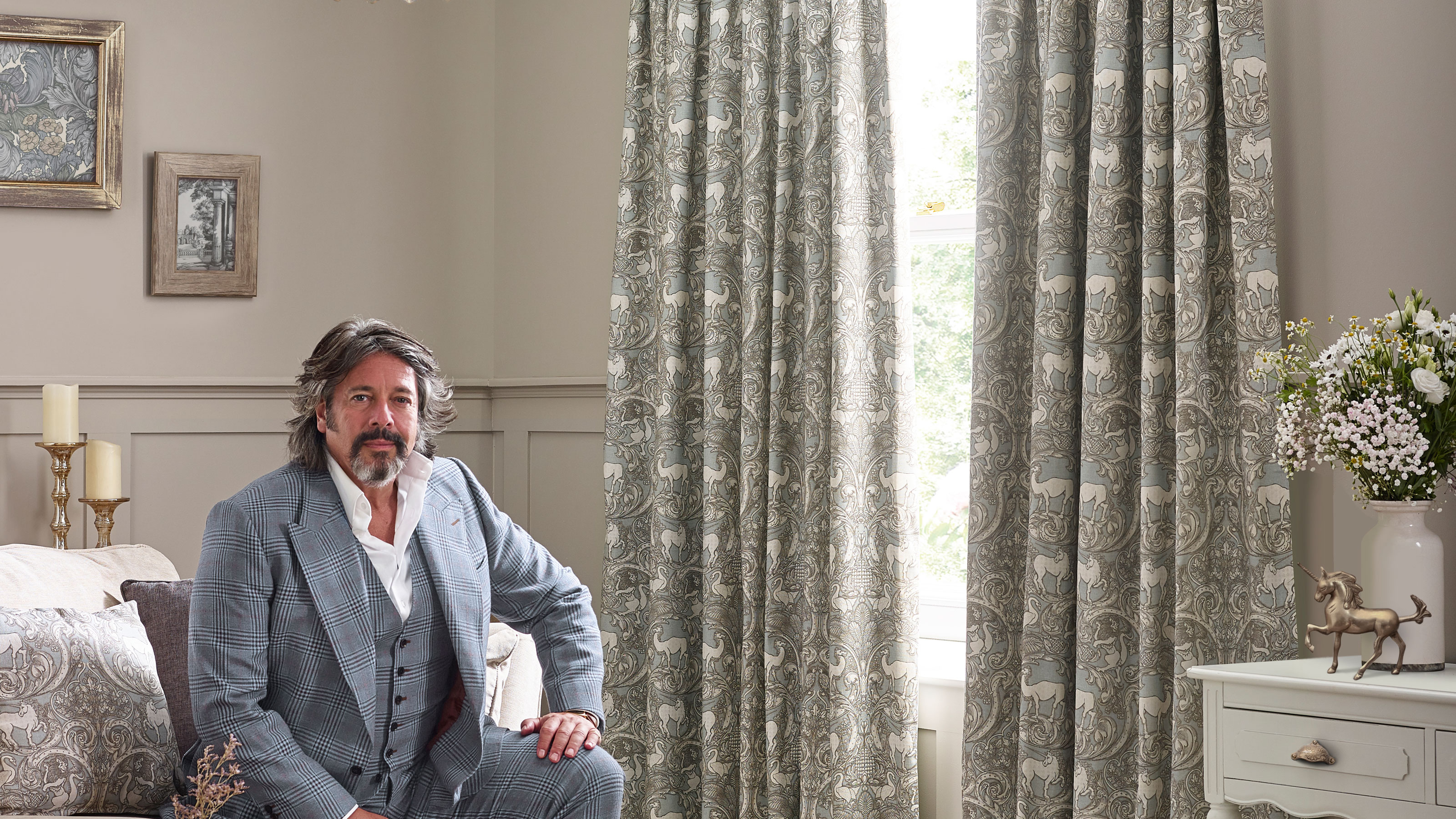 Terry and House Llewelyn-Bowen fabric curtains in grey and light blue hung over a window with a man sat next to them