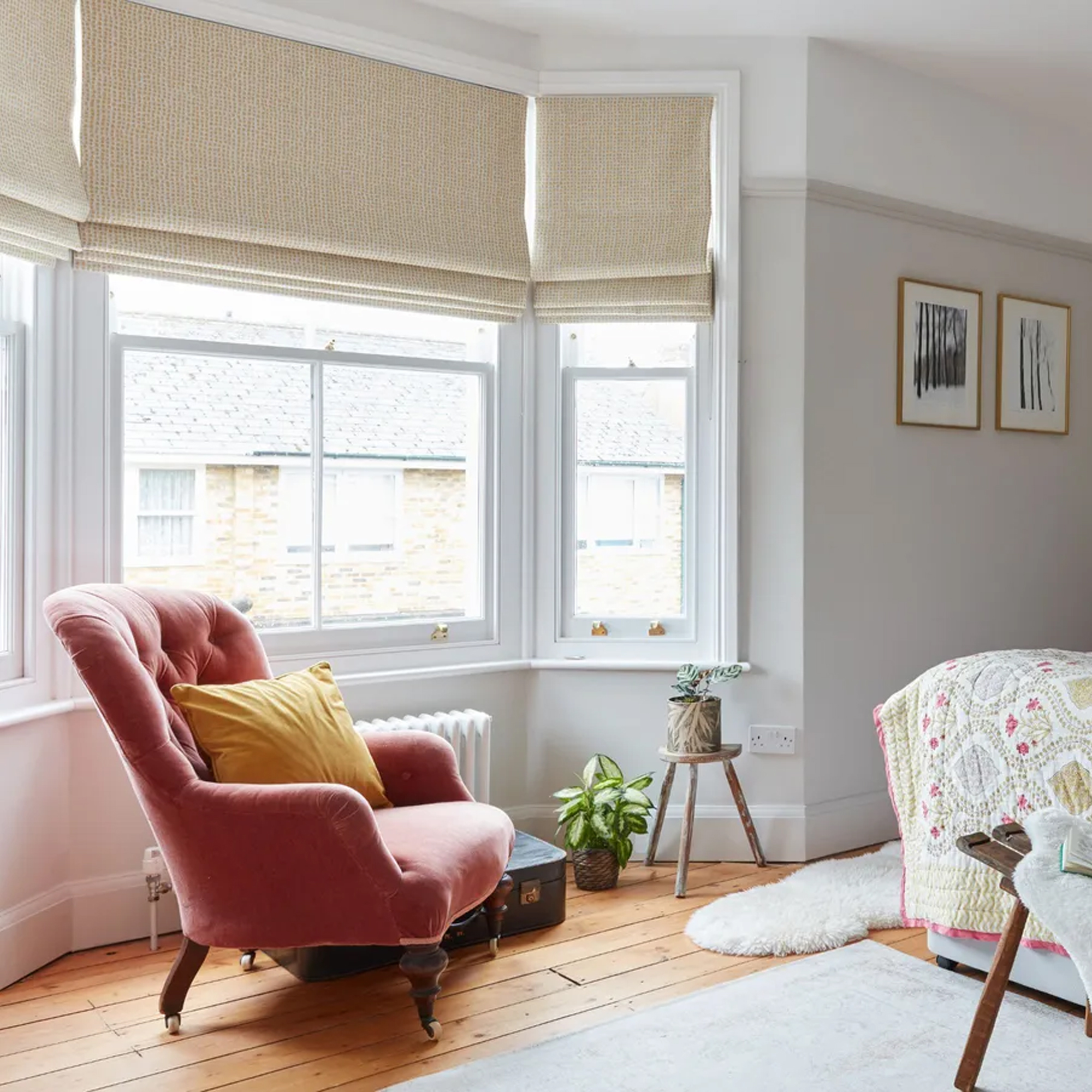 A pink velvet bedroom accent chair in front of a bay window next to a bed covered by a quilt