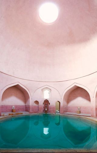 The oldest room in the Rác Thermal Bath. A large in door bath with blue water, pink walls and a domed roof.