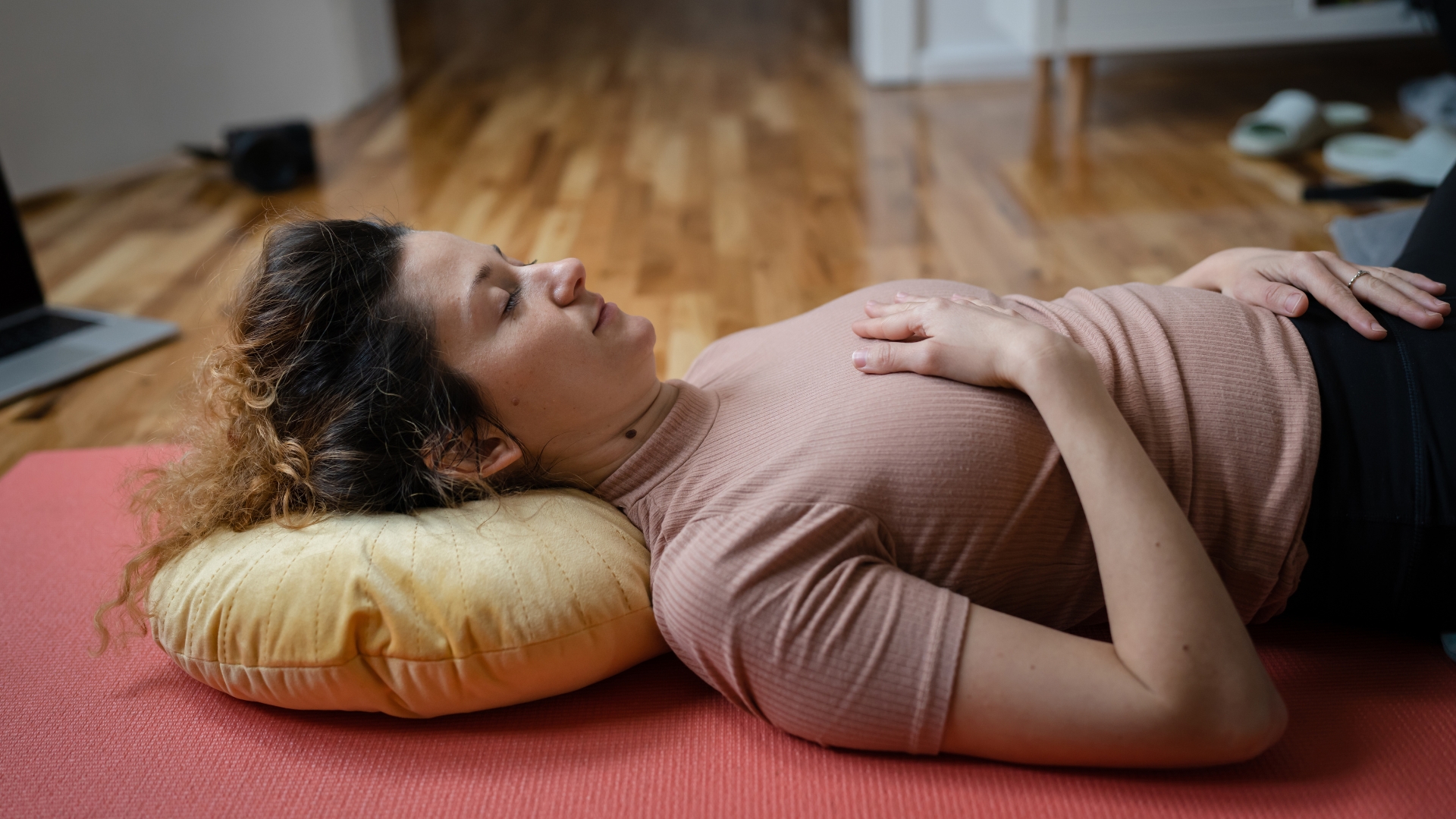 woman lying on her back with a yellow cushion behind her head with one hand on her chest and abdomen.