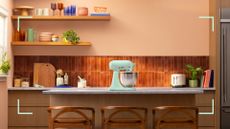 Retro kitchen with brown wall times and mustard yellow painted shelves on peach walls with a KitchenAid mixer on the counter to show KitchenAid colour of the year 2026