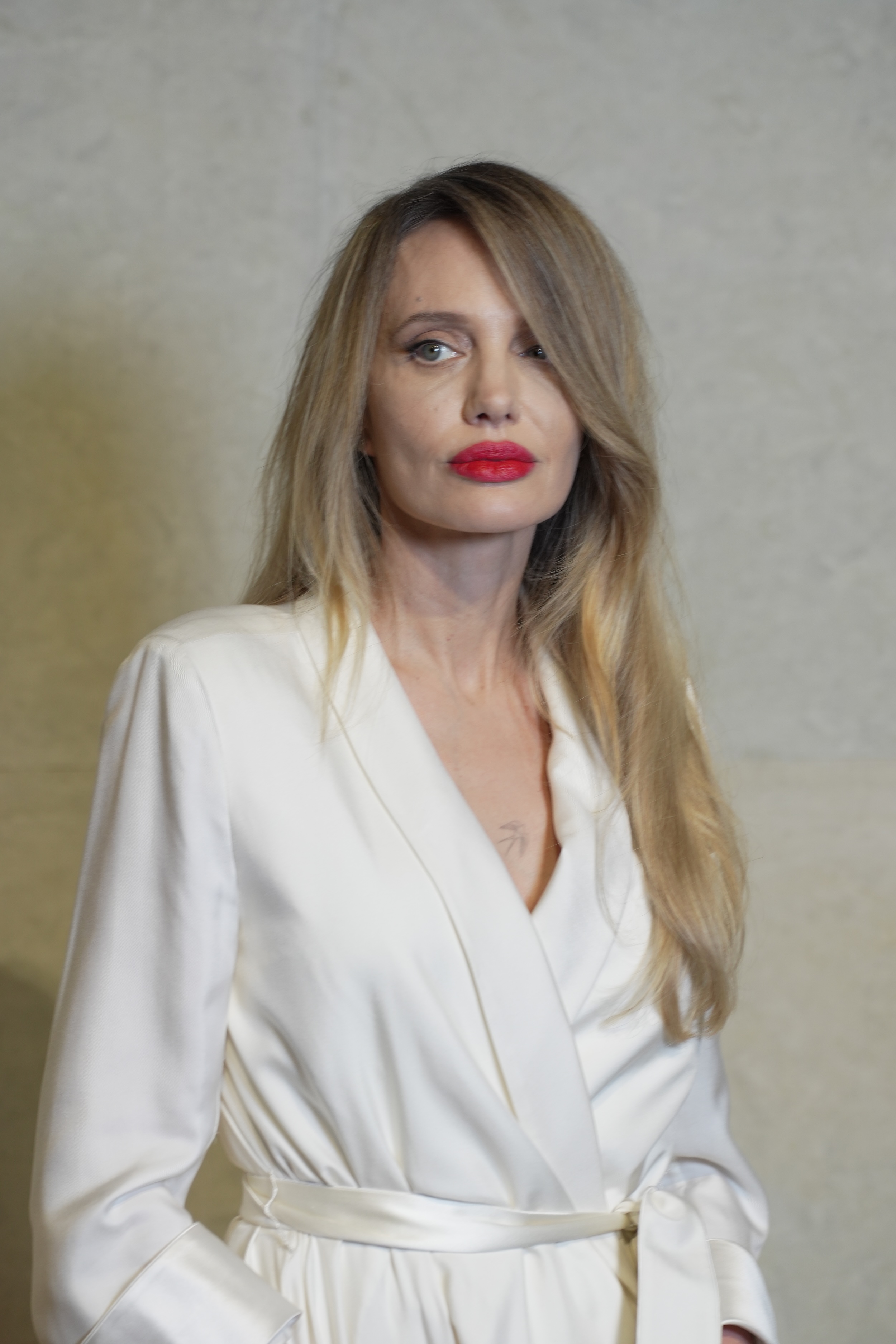 a woman with blonde hair wearing red lipstick and a white blazer