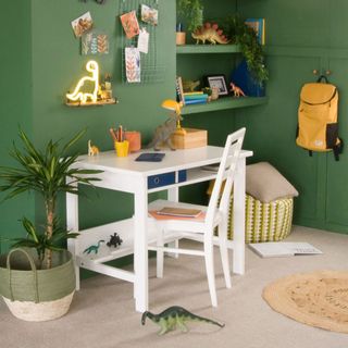 A green painted kids bedroom with white desk and desk chair and dinosaurs dotted around the room