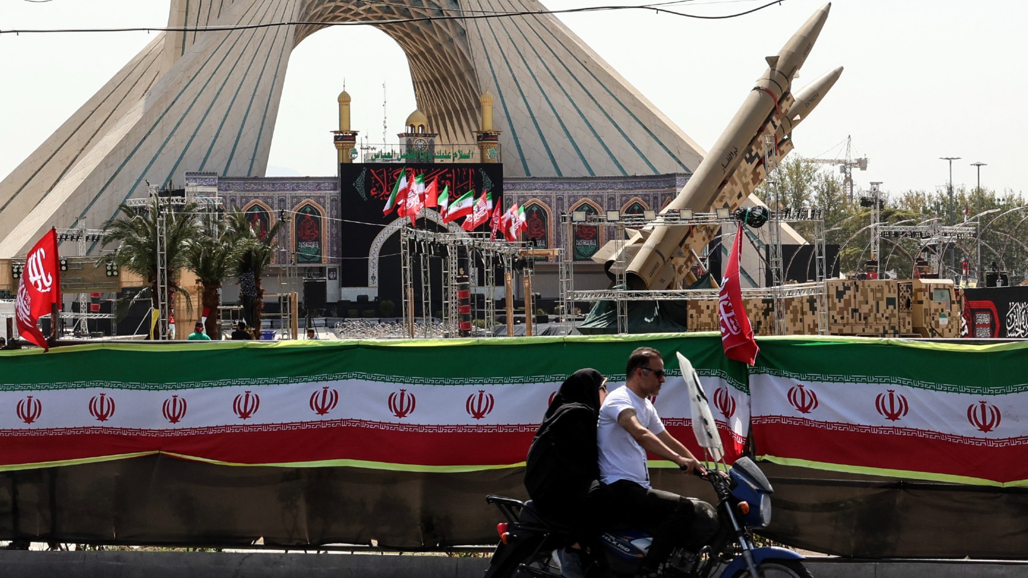 A couple rides by a ballistic missile display in Tehran