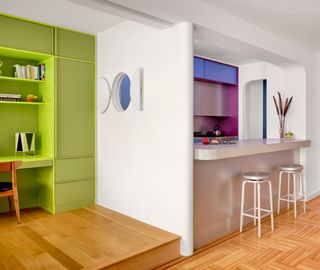 Stainless steel kitchen and green built-in office niche separated by white wall with porthole window in the middle