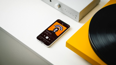 Lifestyle photos showing the Pro-Ject Uni Box S3 on a white unit with a mobile phone playing Massive Attack and a yellow turntable to the right of the amplifier