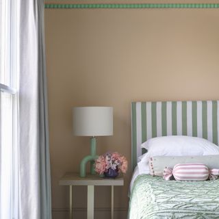 how to decorate a guest room, coral walls with bright green beading, stripe headboard, green bedspread, green lamp on modern side table, flowers