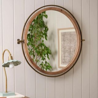 A round mirror on a wooden white wall with a lamp to the left