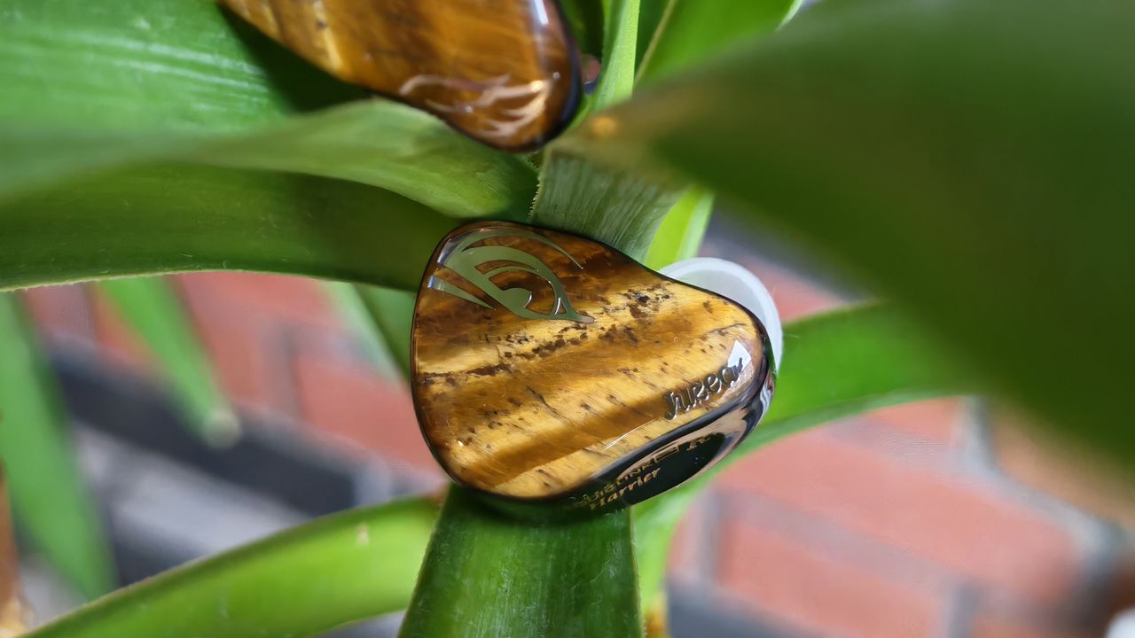 A selection of photos of the Juzear Harrier in-ear monitor, amongst green plants and coffee cups.