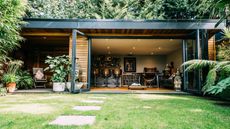 A timber clad garden room with large open glass doors 