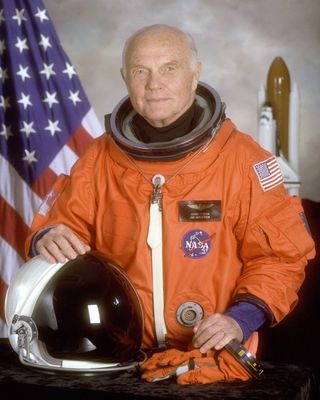 John Glenn NASA portrait where he is wearing an orange NASA spacesuit and rests his right hand on a space helmet.