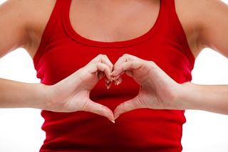 A woman holds her hands in a heart shape in front of her chest.