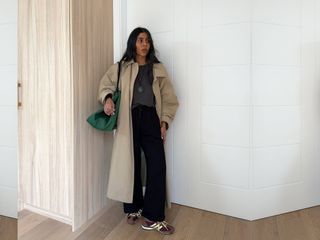 Stylist Monikh Dale wearing a fall outfit including a classic Toteme trench coat, grey t-shirt, black pants, green The Row tote bag, and Adidas SL72 sneakers.