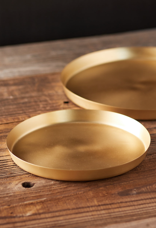 two round gold plant trays on a wooden surface
