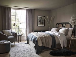 bedroom with a black head board and corner armchair with neutral colours and soft textures