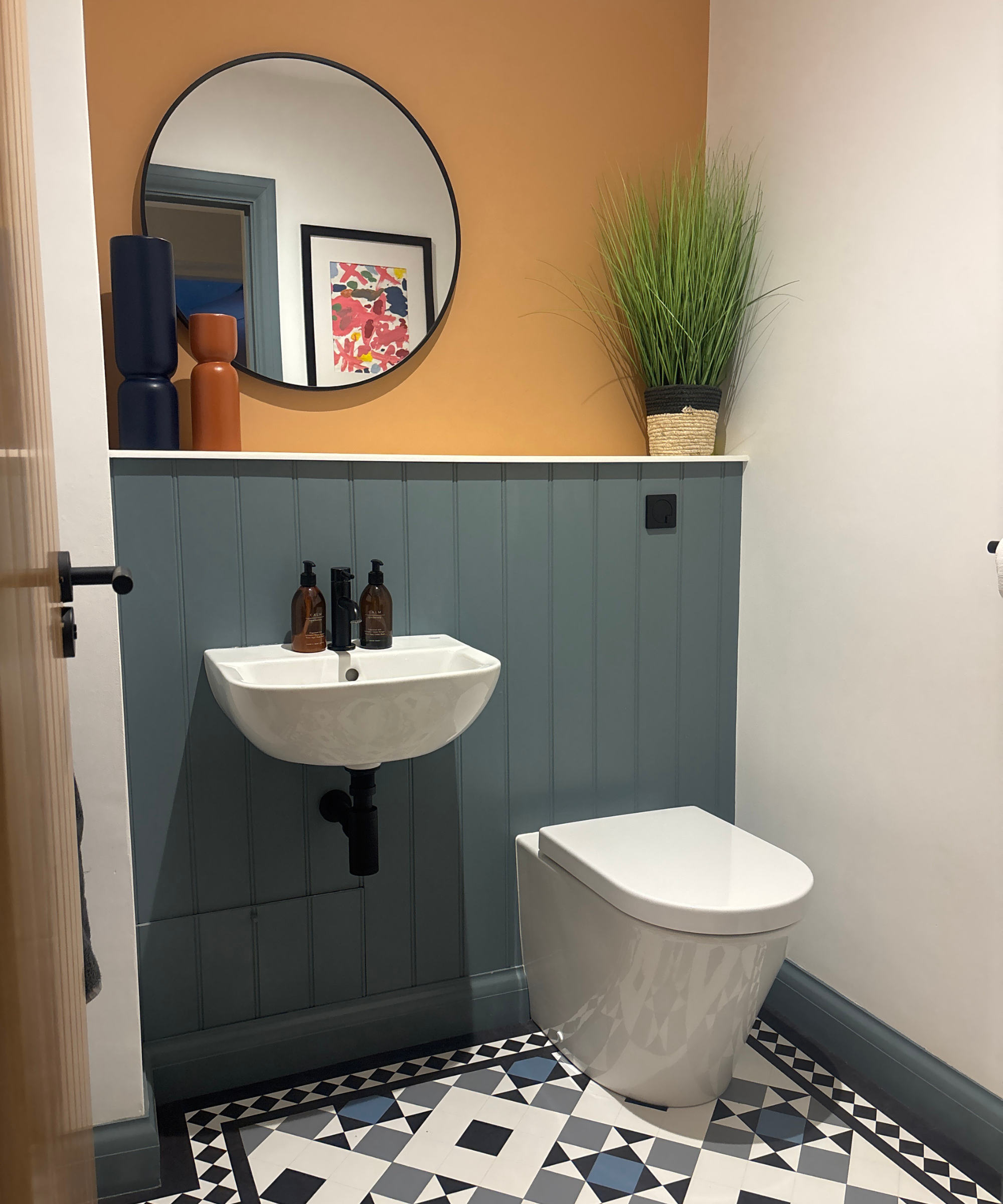 Toilet room with blue patterned flooring, half blue panelled wall and mustard paint above with a circular mirror