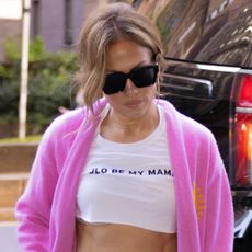 Jennifer Lopez wearing a slogan crop top with a pink cardigan slouchy jeans and a dior wicker bag