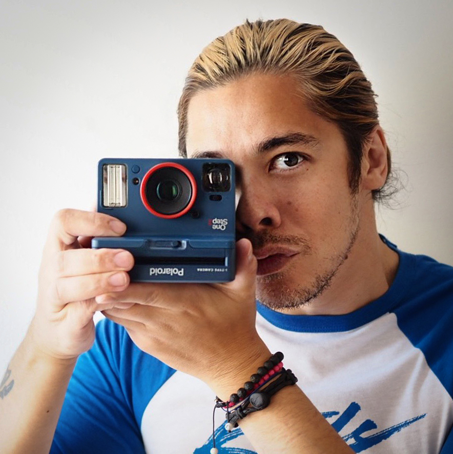 James Artaius wearing a blue baseball shirt holding a Polaroid Stranger Things camera