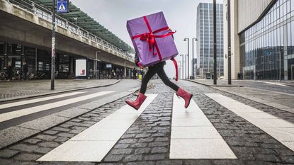 A person carrying a huge wrapped gift runs across a street.