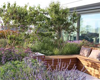 Roof garden ideas illustrated with meadow style planting and built-in L shaped wooden bench seating.