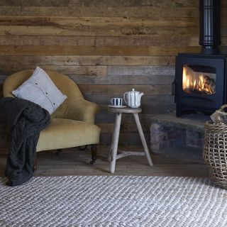 fire place with wooden wall armchair with pillow and throw table with teapot and cup