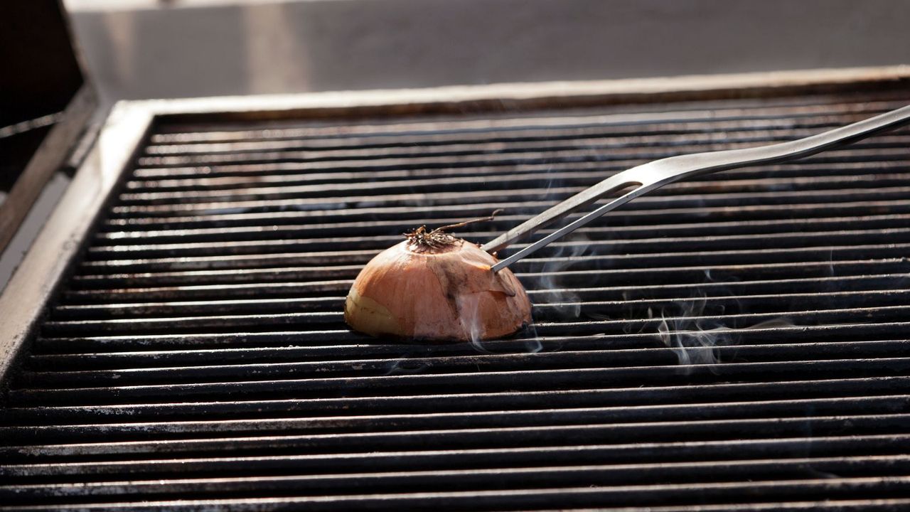 A mean attempting to clean a grill with an onion