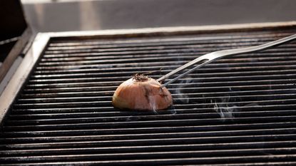 A mean attempting to clean a grill with an onion