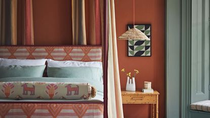 Wall decor for bedroom, featuring terracotta colored walls with gray-blue window frames and shutters and geometric print wall art, headboard and soft furnishings.