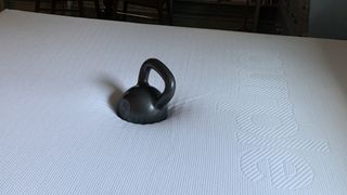 A black kettlebell placed on top of the Purple Plus mattress during review testing