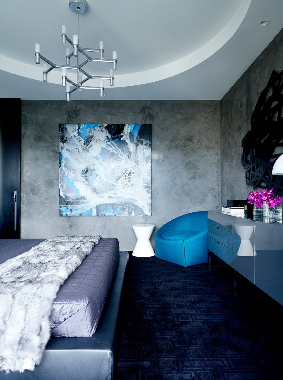 A bedroom with black carpet, a bright blue chair, and textured walls, with a large art work on the wall