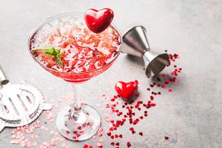 A valentine's margarita cocktail with red hearts, red heart confetti and a cocktail shot measurer.