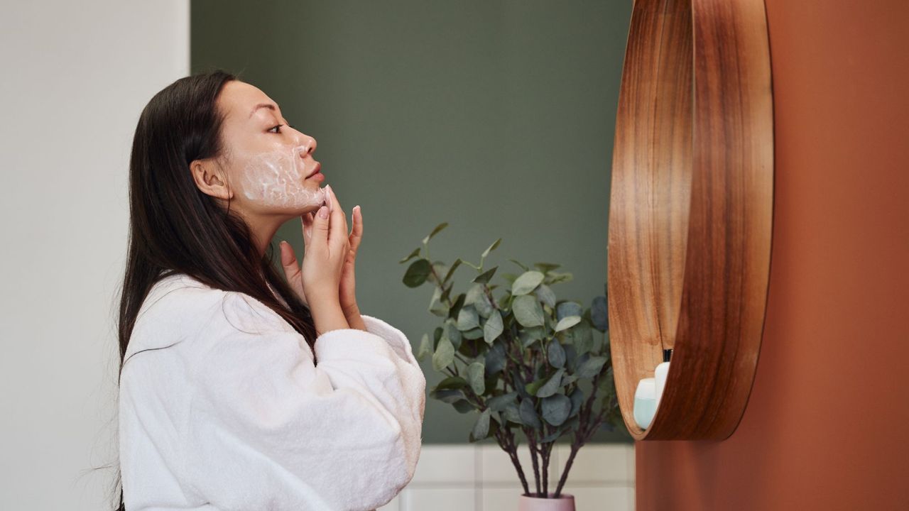 Simple skincare routine - woman looking in mirror applying face cream