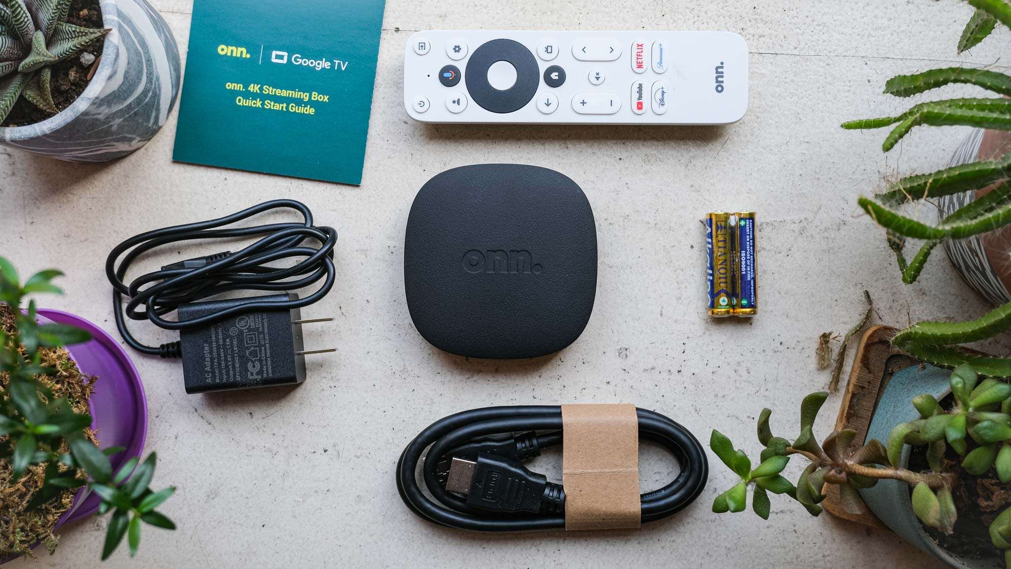 Streaming box on Google TV 4K onn center (clockwise from top) remote control, its battery, HDMI cord, power adapter and quick start guide