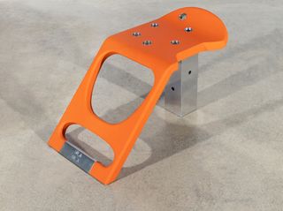 A stool with sloping orange seat and metal base, designed by Samuel Ross